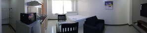 A compact room with a kitchenette, a bed, a chair, and a painting on the wall.