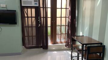 A room with a sliding glass door, a flat-screen TV mounted on the wall, and a wooden table with a chair.