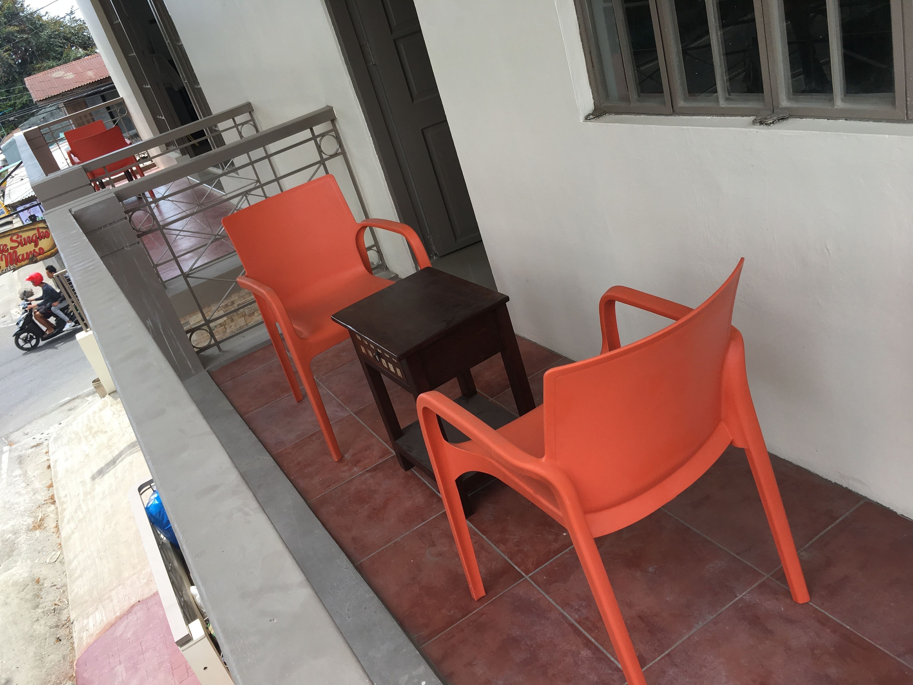 Un balcon avec deux chaises en plastique orange et une petite table en bois.