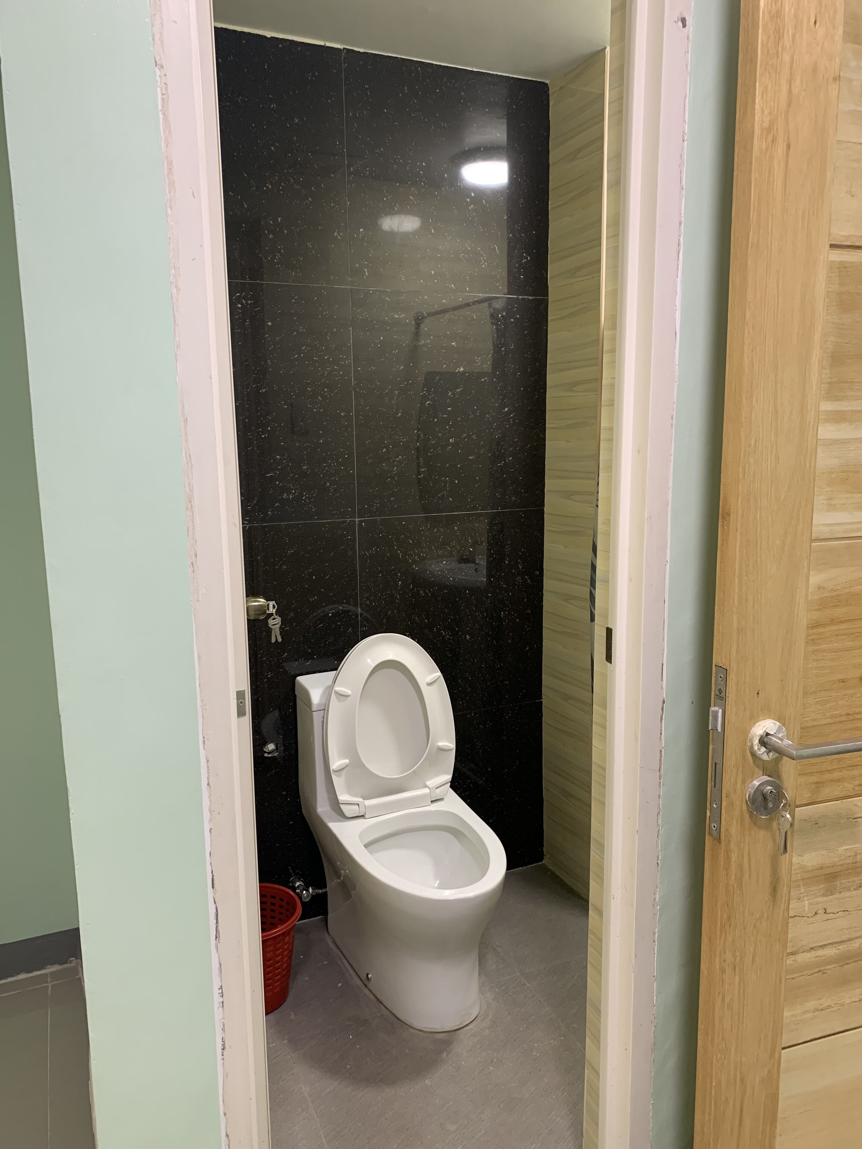 Un baño pequeño con inodoro blanco, paredes de azulejos negros y una puerta de madera.