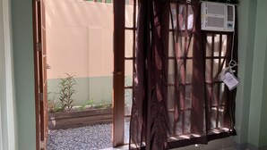 Una habitación con puerta de vidrio corrediza que da a un balcón, una ventana con cortina y un equipo de aire acondicionado en la pared.