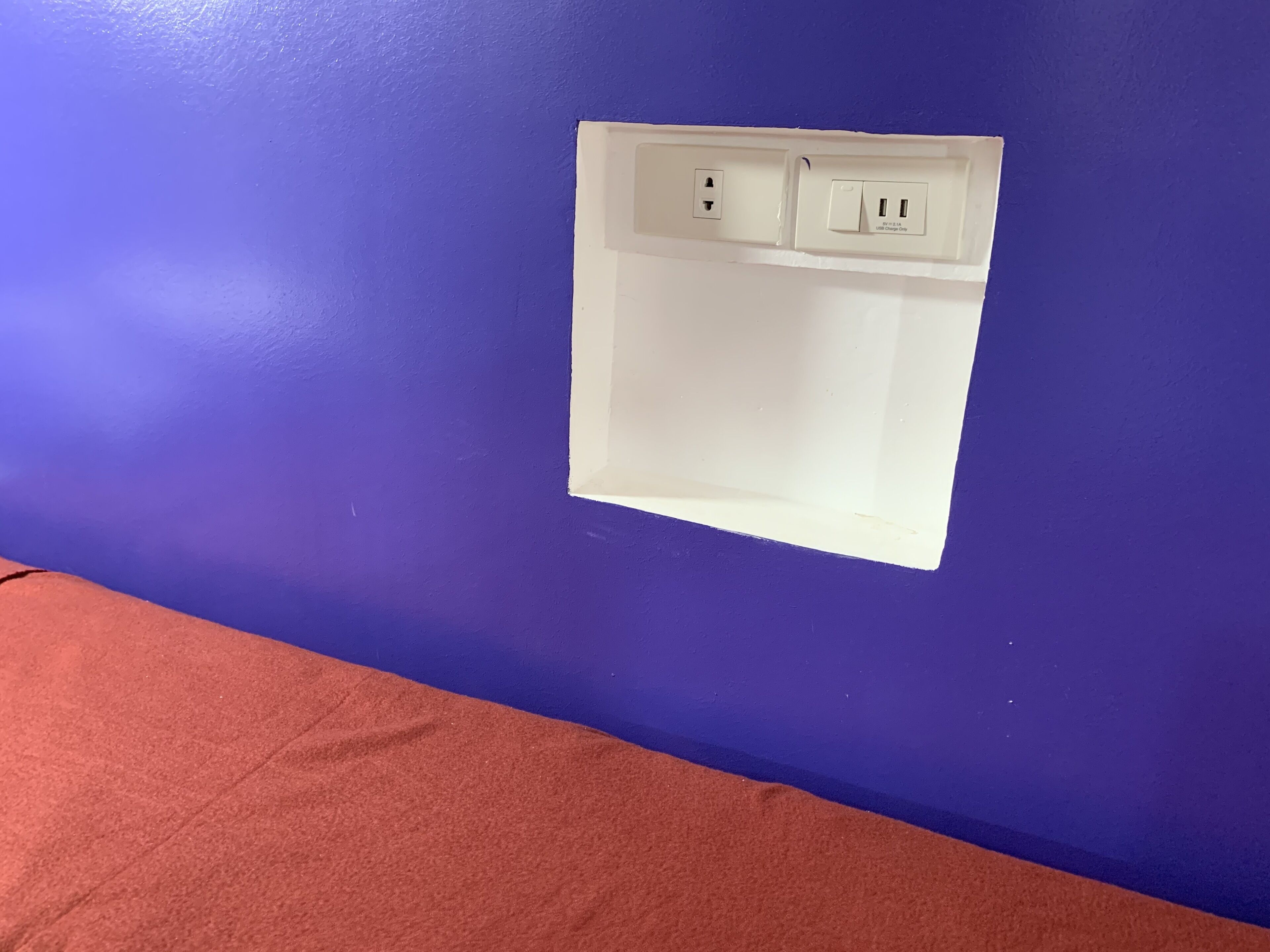 Eine Wand in Lila mit einer weißen Steckdosenabdeckung.