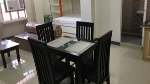 Habitación pequeña con literas, una mesita con sillas, ventana con aire acondicionado y suelo de baldosas.