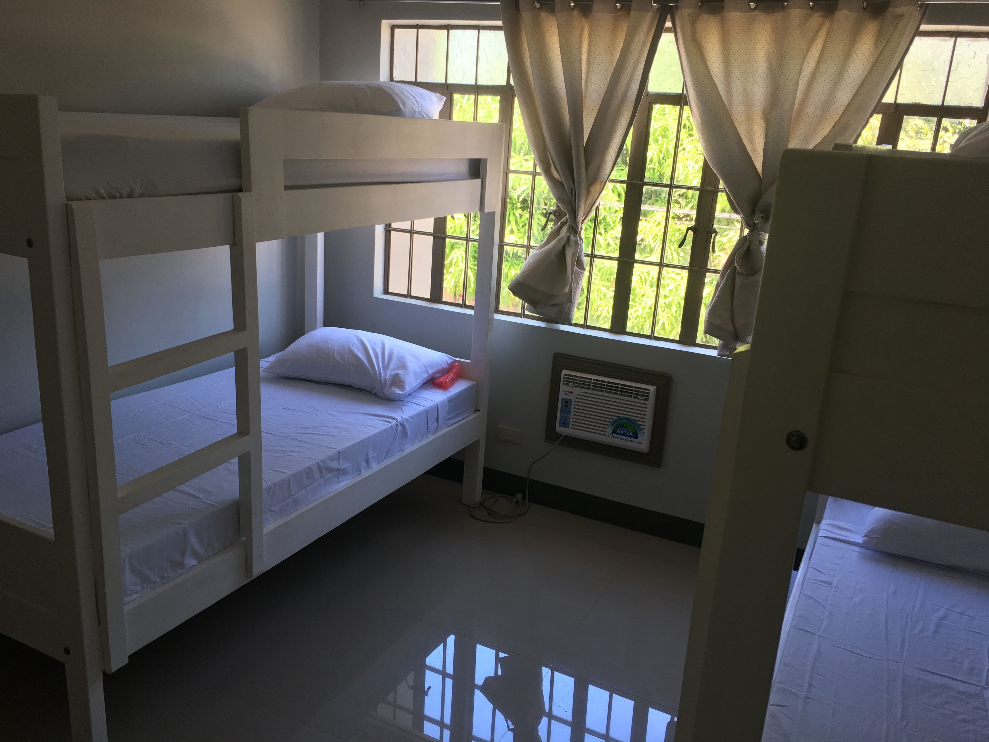 Dormitorio con literas, ventana, cortinas e aire acondicionado instalado en la pared.