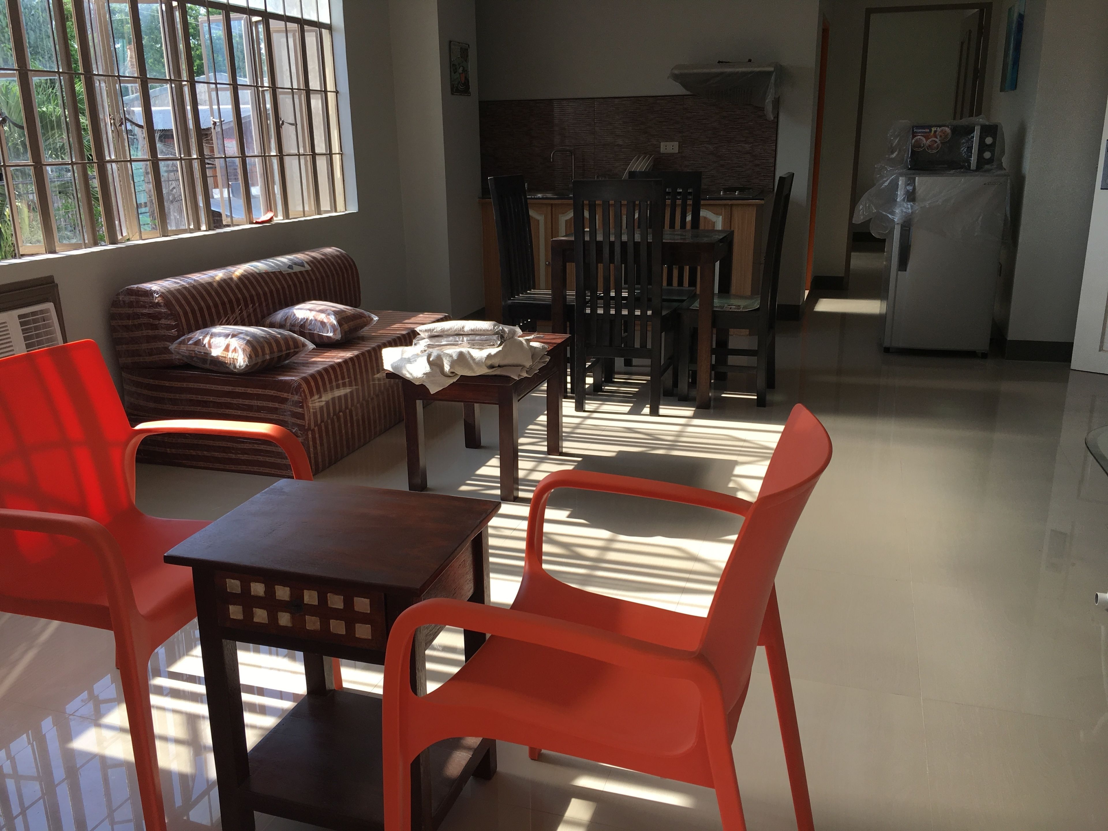 A living room with a sofa, a dining table with chairs, a kitchen area, and a refrigerator.