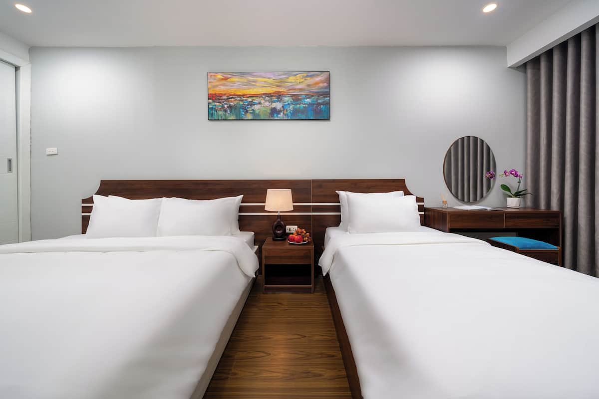 Une chambre d’hôtel avec deux lits, une table de chevet avec une lampe, un tableau au mur et une vue sur l’extérieur.
