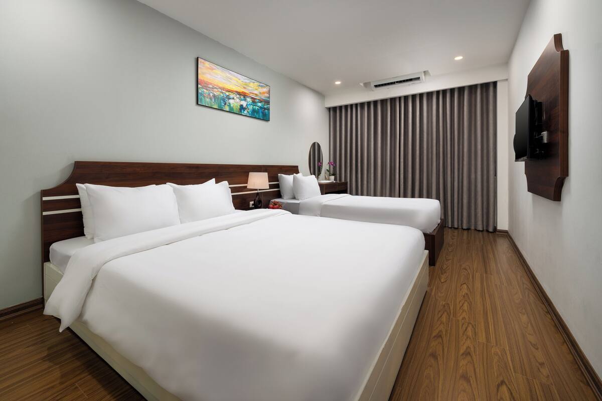 Une chambre d’hôtel avec deux lits, un téléviseur à écran plat fixé au mur et une grande fenêtre avec des rideaux.