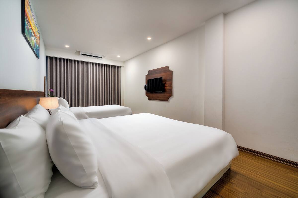 Une chambre d’hôtel avec un grand lit, un téléviseur à écran plat fixé sur un panneau en bois et une fenêtre avec des rideaux.