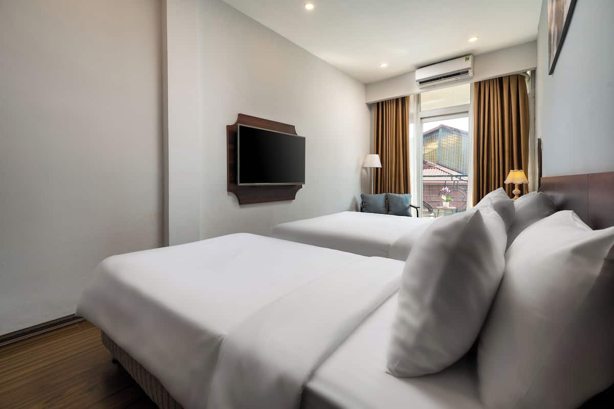 Une chambre d’hôtel avec deux lits, un téléviseur à écran plat fixé au mur, une fenêtre avec des rideaux et une lampe sur la table de chevet.