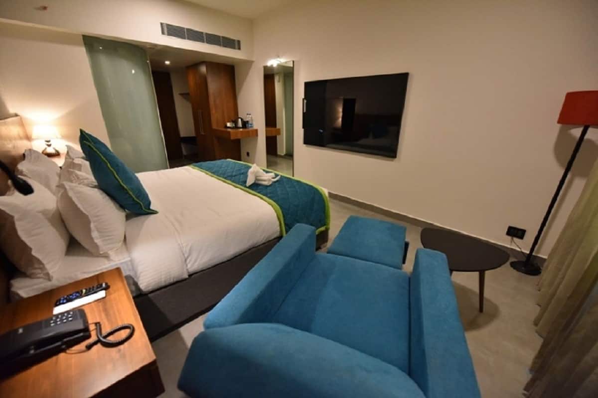 A hotel room with two beds, a desk with a remote control, a TV on the wall, and a floor lamp.