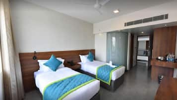 A hotel room with two beds, a wooden headboard, a desk, and a bathroom visible through a glass door.