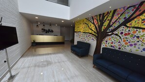 Un hall d’entrée spacieux comprenant un comptoir d’accueil, une grande fresque murale et des espaces détente.
