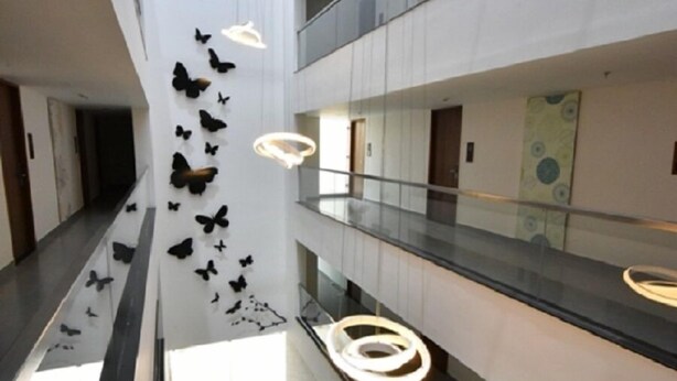 Un intérieur moderne doté d’un atrium central, de rampes en verre et d’une installation artistique murale en forme de papillon.
