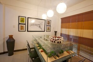 Un intérieur moderne avec une table vitrée servant de présentoir, des œuvres d’art encadrées accrochées au mur et un grand vase.