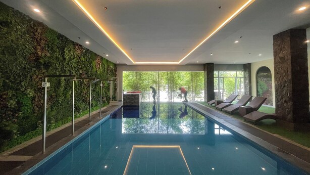 An indoor swimming pool with a glass barrier, a green wall with plants, and a view of trees outside. - Via Appia Tagaytay (Tagaytay)