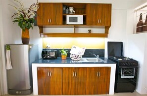 Une cuisine compacte dotée d’armoires en bois, d’un four à micro-ondes, d’un grille-pain, d’un évier, d’une cuisinière et d’un réfrigérateur.