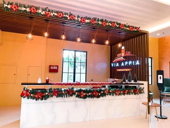 Un comptoir d’accueil décoré d’une guirlande de Noël, une enseigne indiquant « Hôtel Via Appia Tagaytay » et un haut-parleur sur la droite.