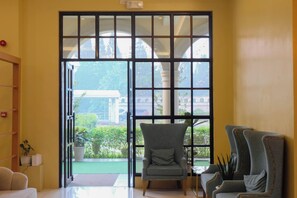 A room with a large sliding glass door leading to a garden, a grey armchair, and a wooden shelf with plants. - Via Appia Tagaytay (Tagaytay)