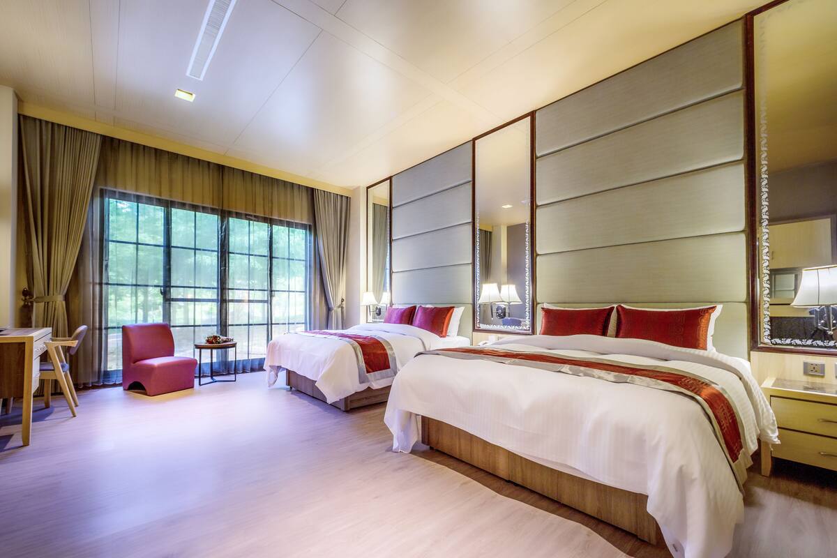 Une chambre d’hôtel avec deux lits, un bureau, une chaise et de grandes fenêtres.