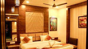 Una habitación de hotel con una cama grande, un ventilador de techo, un ventanal con persianas, un cuadro en la pared y un espejo sobre la cama.