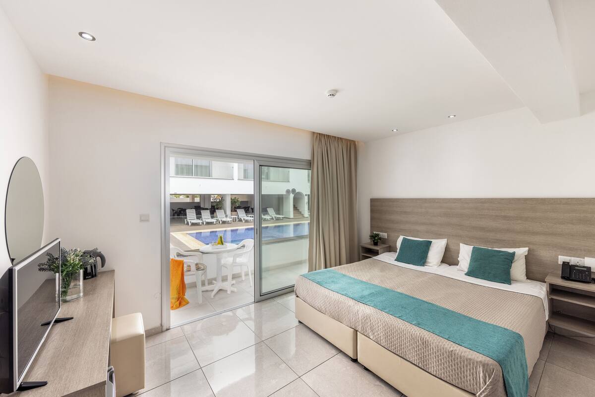 Une chambre d’hôtel moderne dotée d’un grand lit, d’un bureau, d’une télévision et offrant une vue sur l’espace piscine.