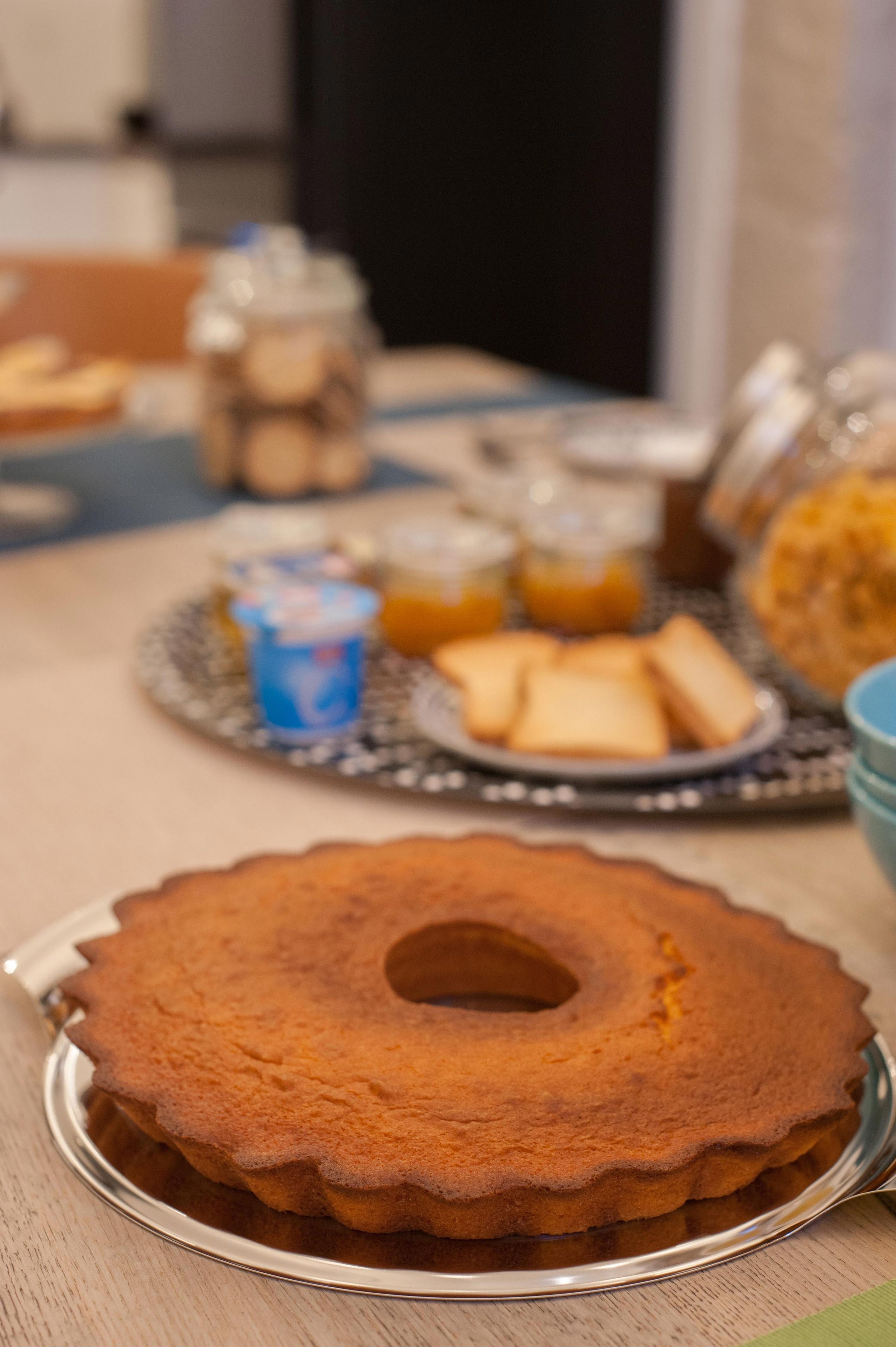 A cake on a silver cake stand with a blurred background of a table with various food items.