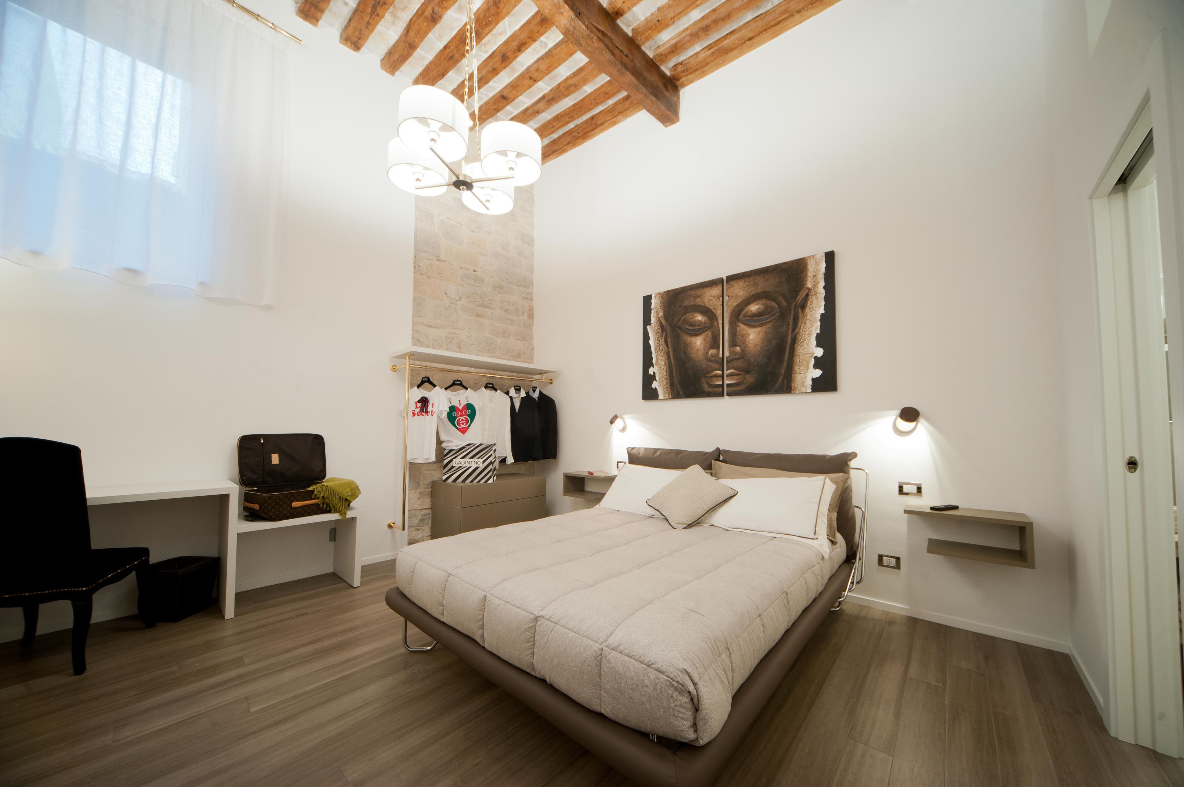 Un dormitorio con cama, mesitas de noche, una silla, armario y una obra de arte colgada en la pared.