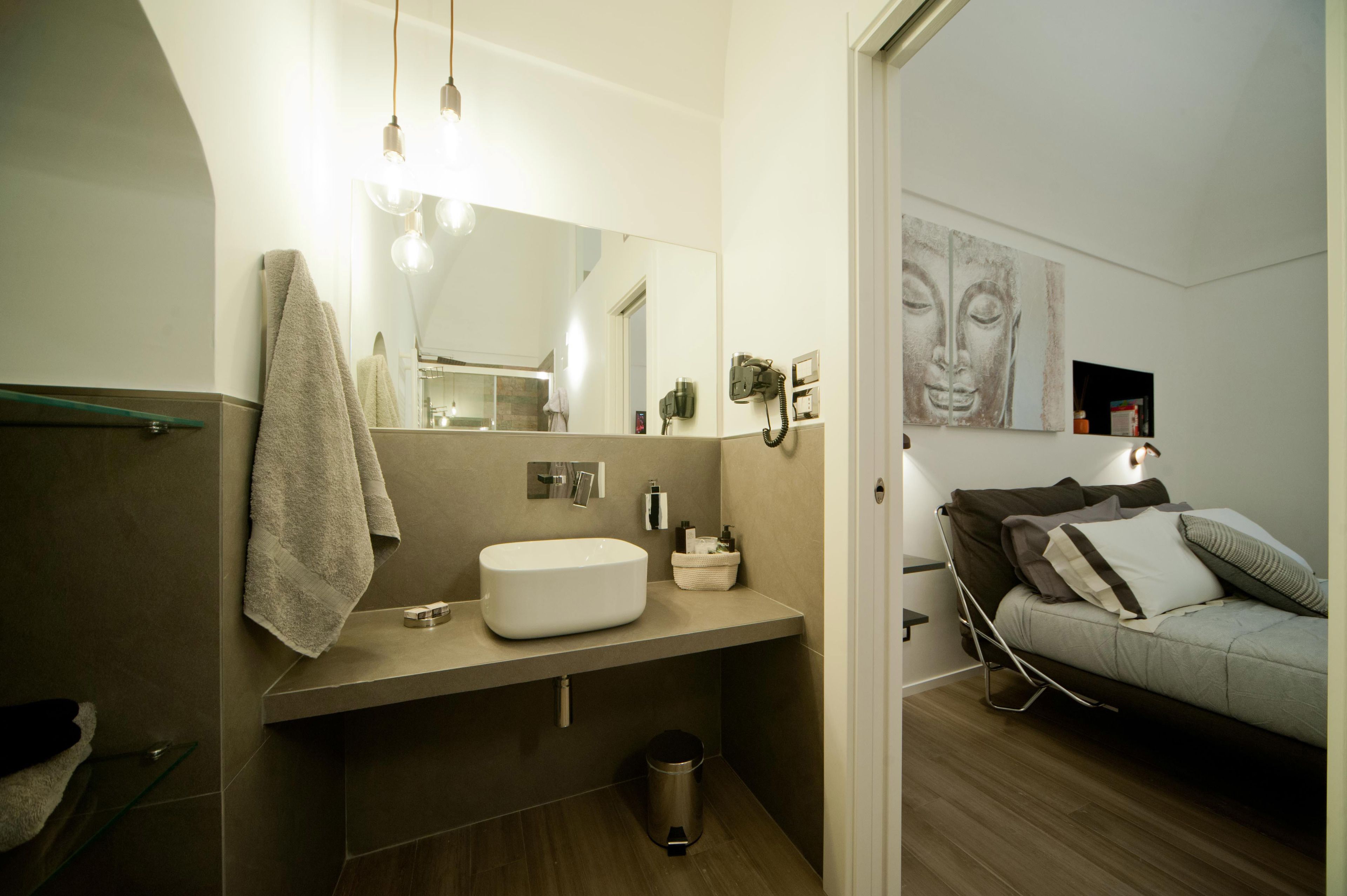 Un baño moderno con un espejo grande, un lavabo y un perchero para toallas. Hay un pequeño cubo de basura debajo del lavabo.