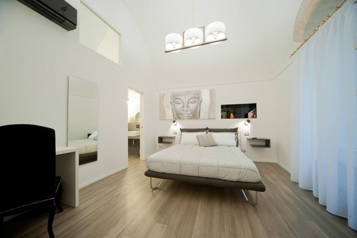 Un dormitorio moderno con cama, mesitas de noche, un escritorio y un espejo grande.