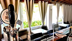A bar area with a beer tap, a menu, and a view of greenery outside. - The Mathraki Studios Adult Only (Corfu)
