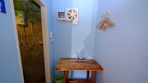 A small bathroom with a wooden table, a heater, a fan, and a green trash bin. - Huenhimphu Resort (Phu Phan)