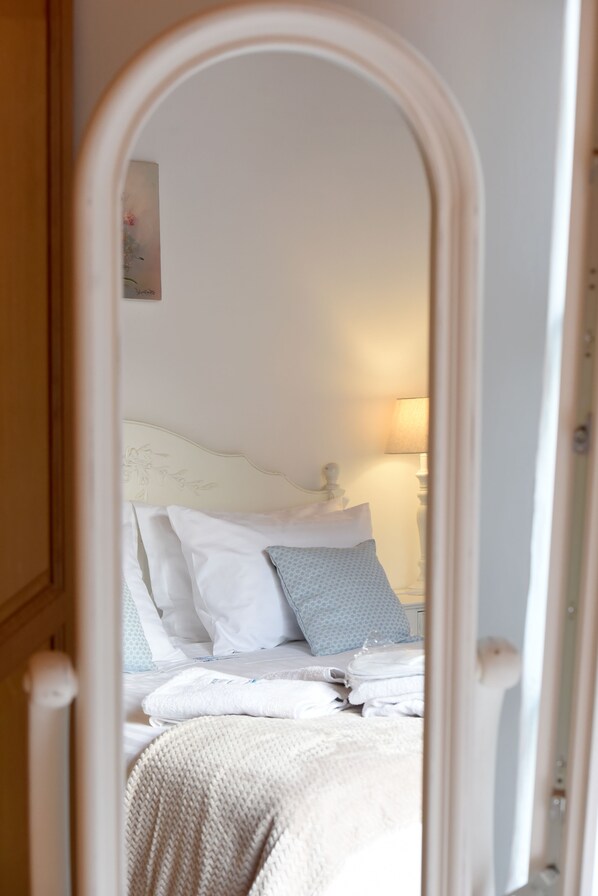 Un dormitorio con cama, almohadas, una lámpara de noche y un espejo.