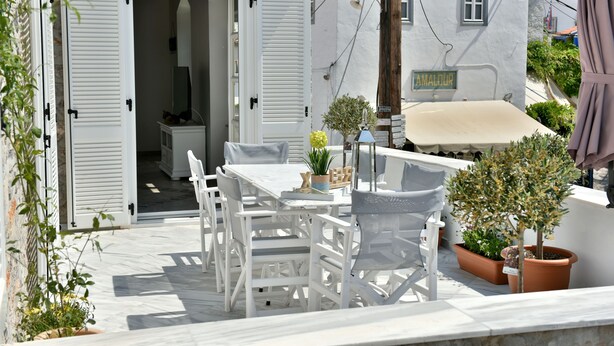 Un espacio de estar exterior blanco con una mesa, sillas, una planta en maceta y un letrero que dice "AMALOUR".
