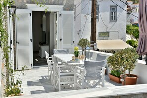 Un espacio de estar exterior blanco con una mesa, sillas, una planta en maceta y un letrero que dice "AMALOUR".