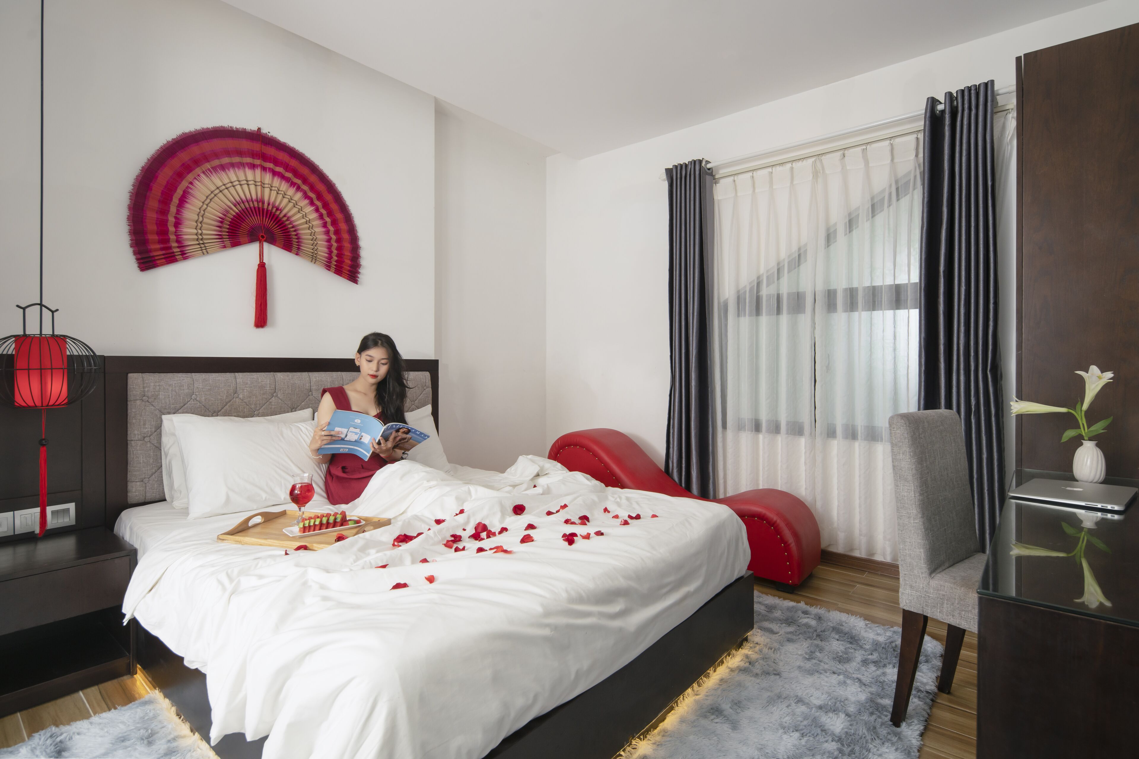 Quarto de hotel com cama, um espaço para leitura, uma mesa de trabalho e janela com cortinas.