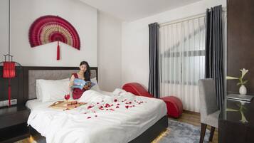 Quarto de hotel com cama, um espaço para leitura, uma mesa de trabalho e janela com cortinas.
