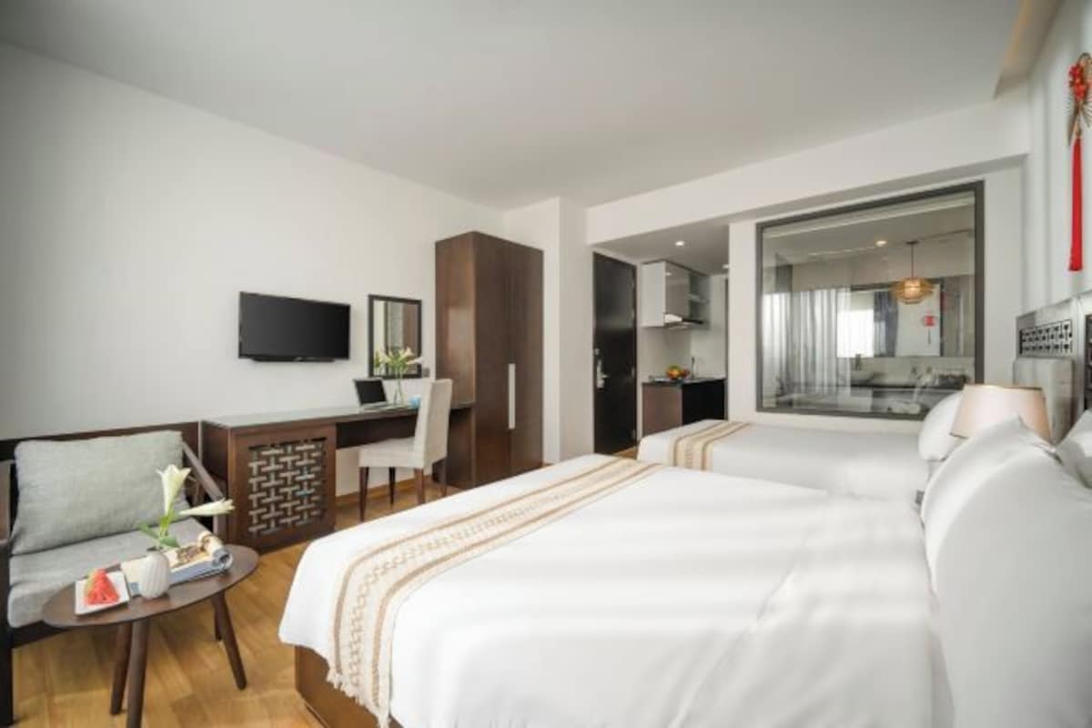 A hotel room with two beds, a desk, a TV, and a seating area with a small table.