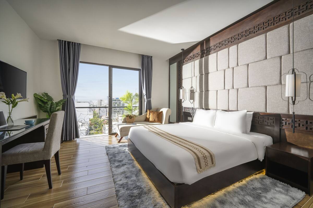 A modern hotel room with a large bed, a desk, and a view of the city.