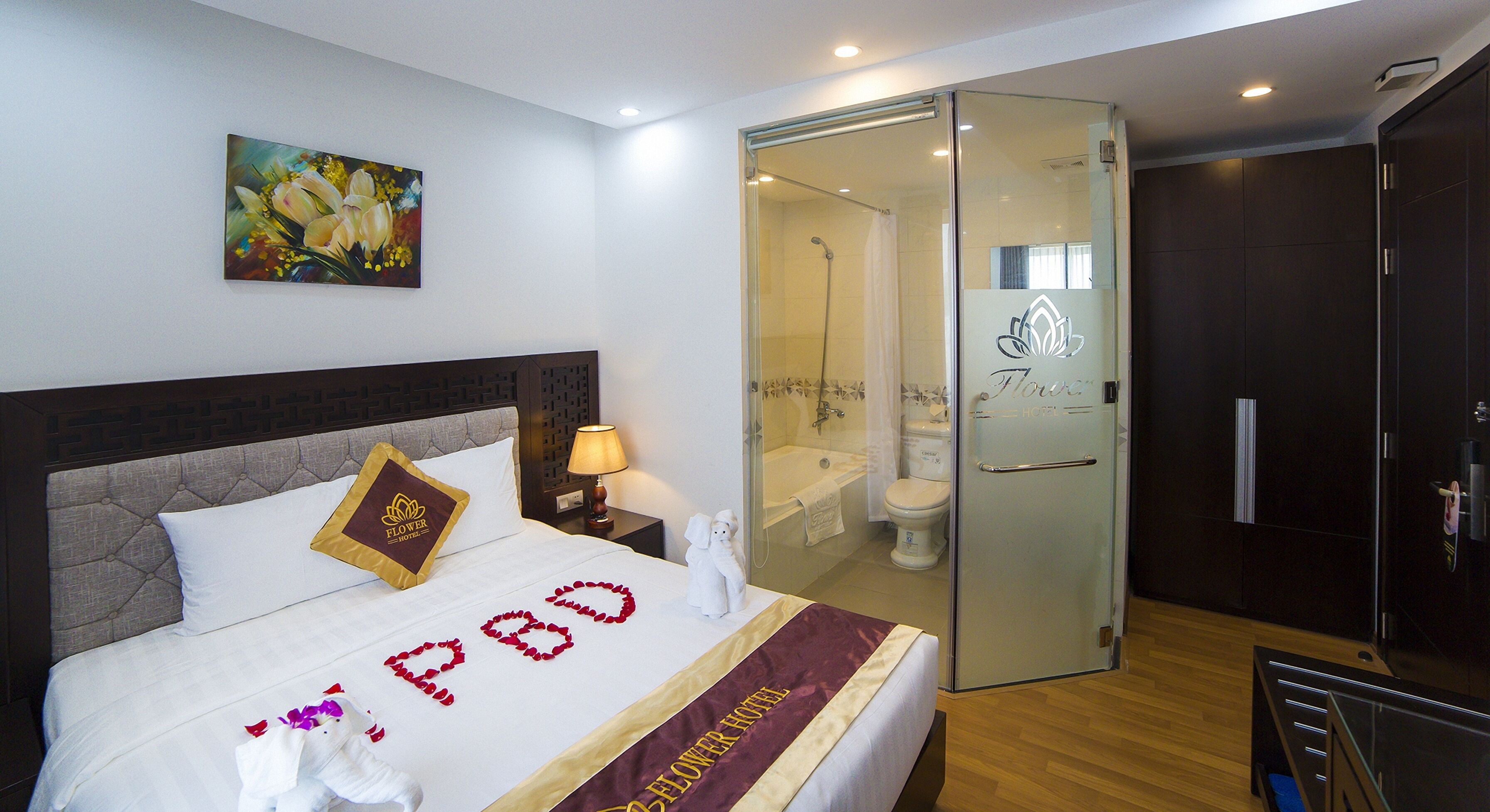 A hotel room with a bed, a painting, a bathroom with a glass door, and a wardrobe.