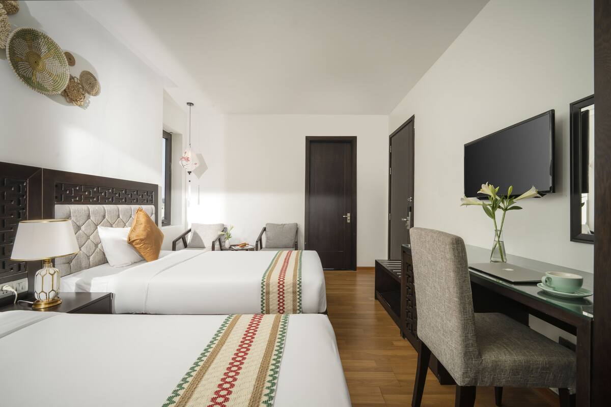 A hotel room with two beds, a desk, a chair, a TV, and a door.