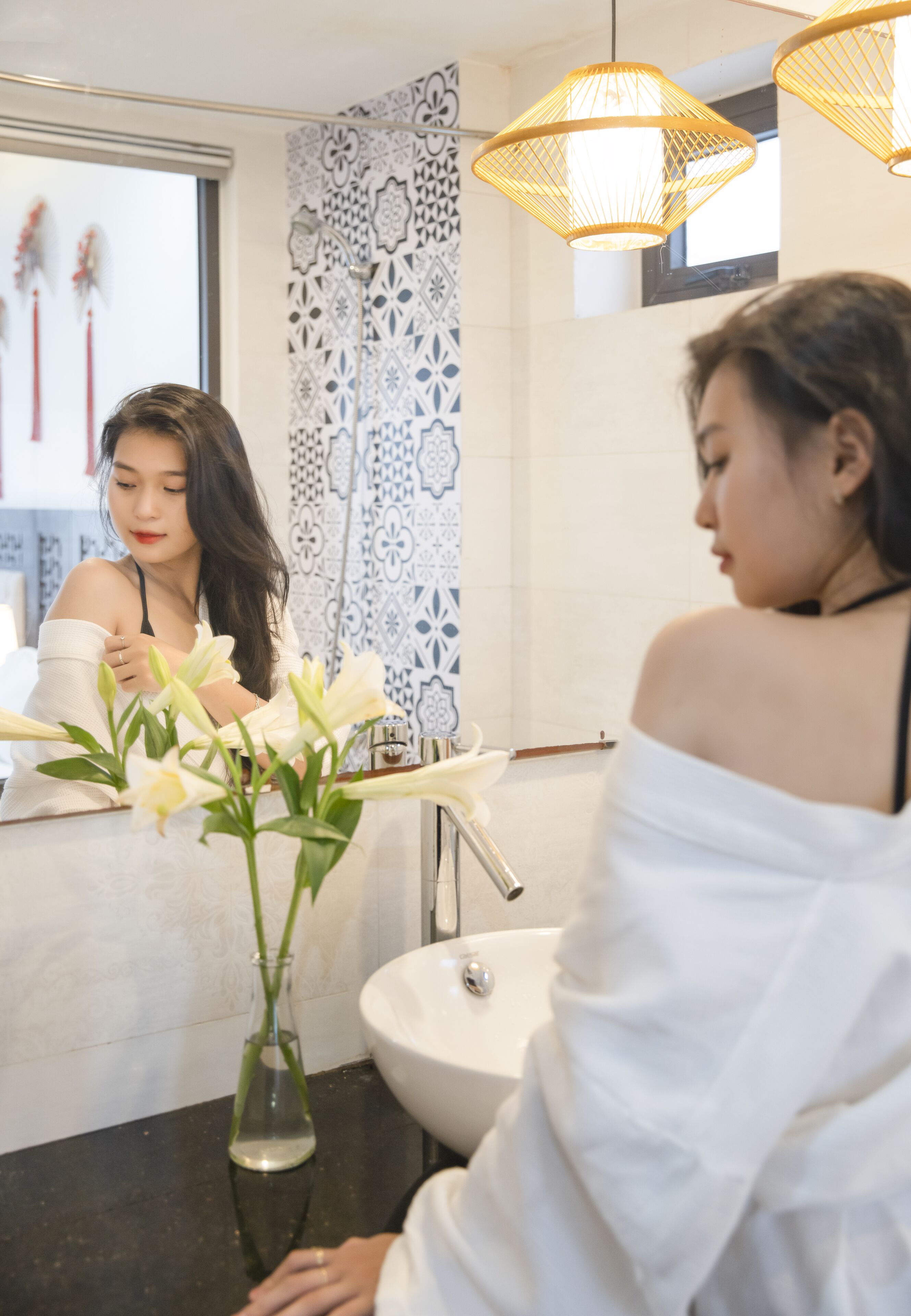 A bathroom with a white sink, a mirror, and a vase with white flowers.