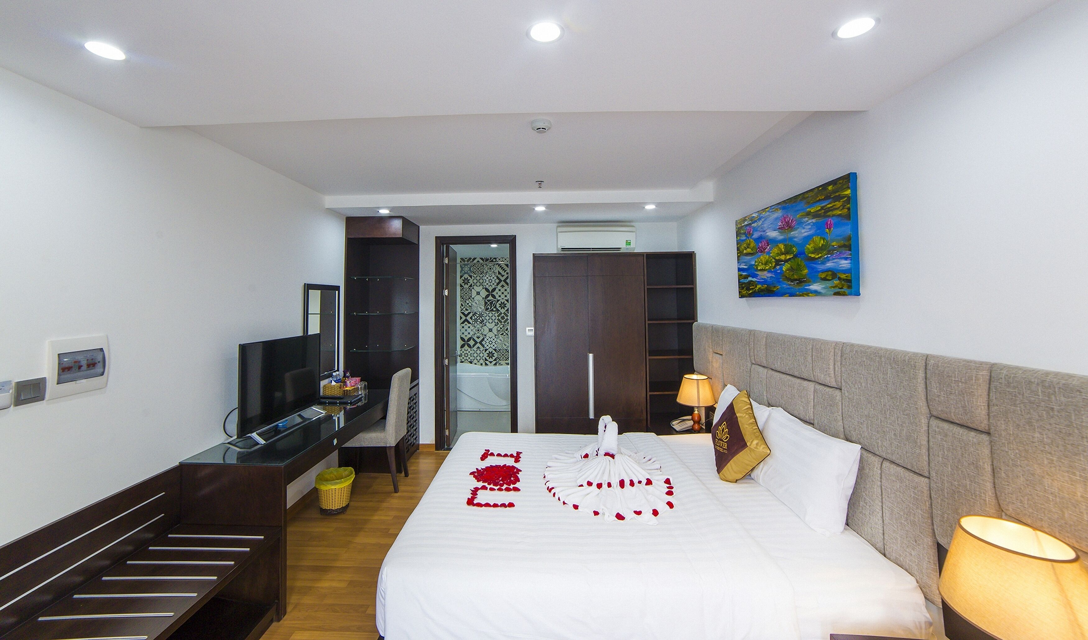 Habitación de hotel con cama, escritorio, silla, televisión, un cuadro y baño visible a través de una puerta abierta.