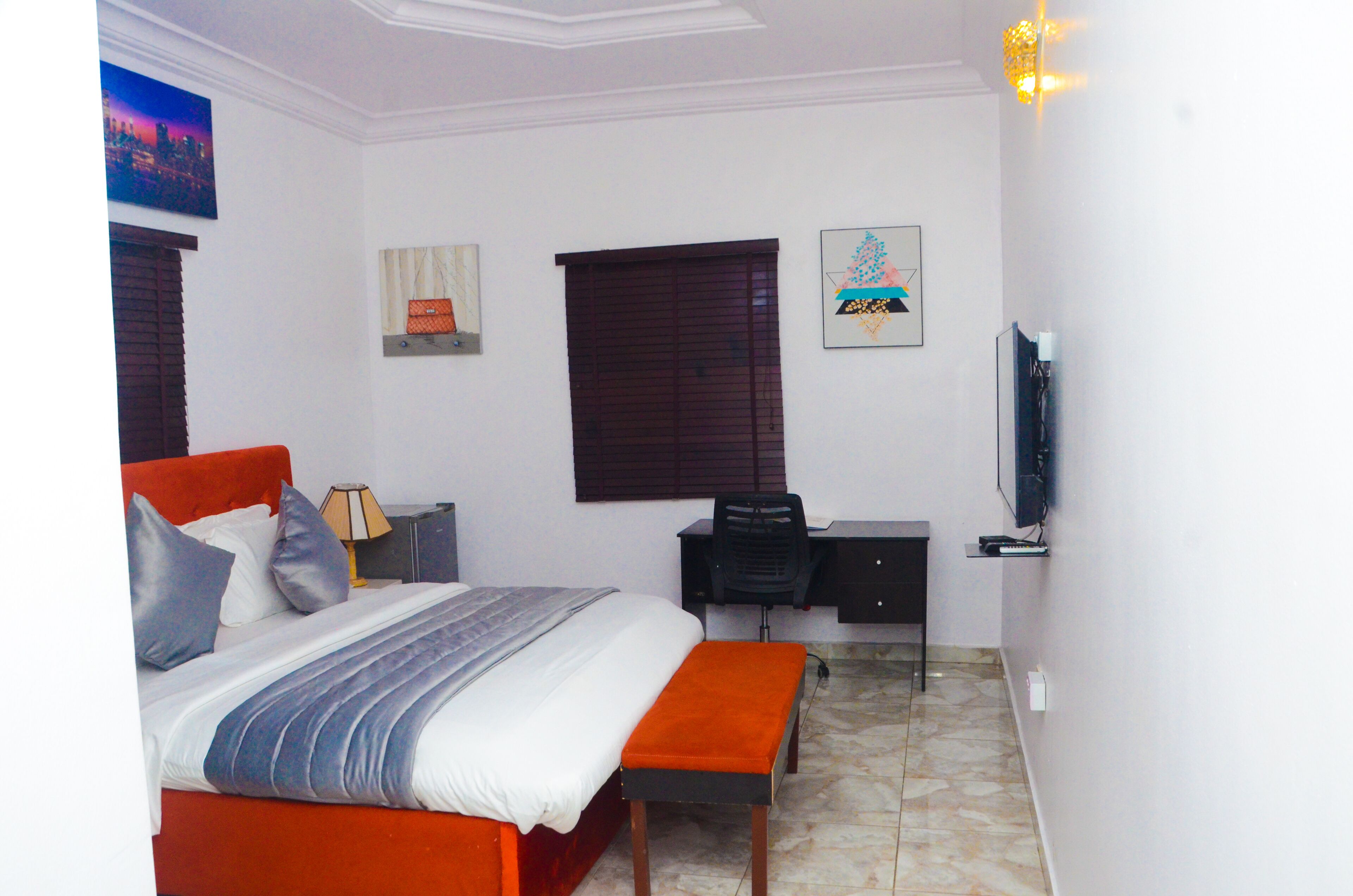 A bedroom with a bed, a desk, a chair, a television, and artwork on the walls.