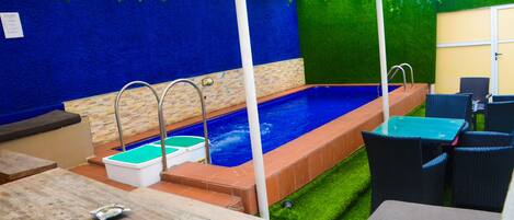 An outdoor pool area with a blue wall, green artificial grass, and wicker furniture.