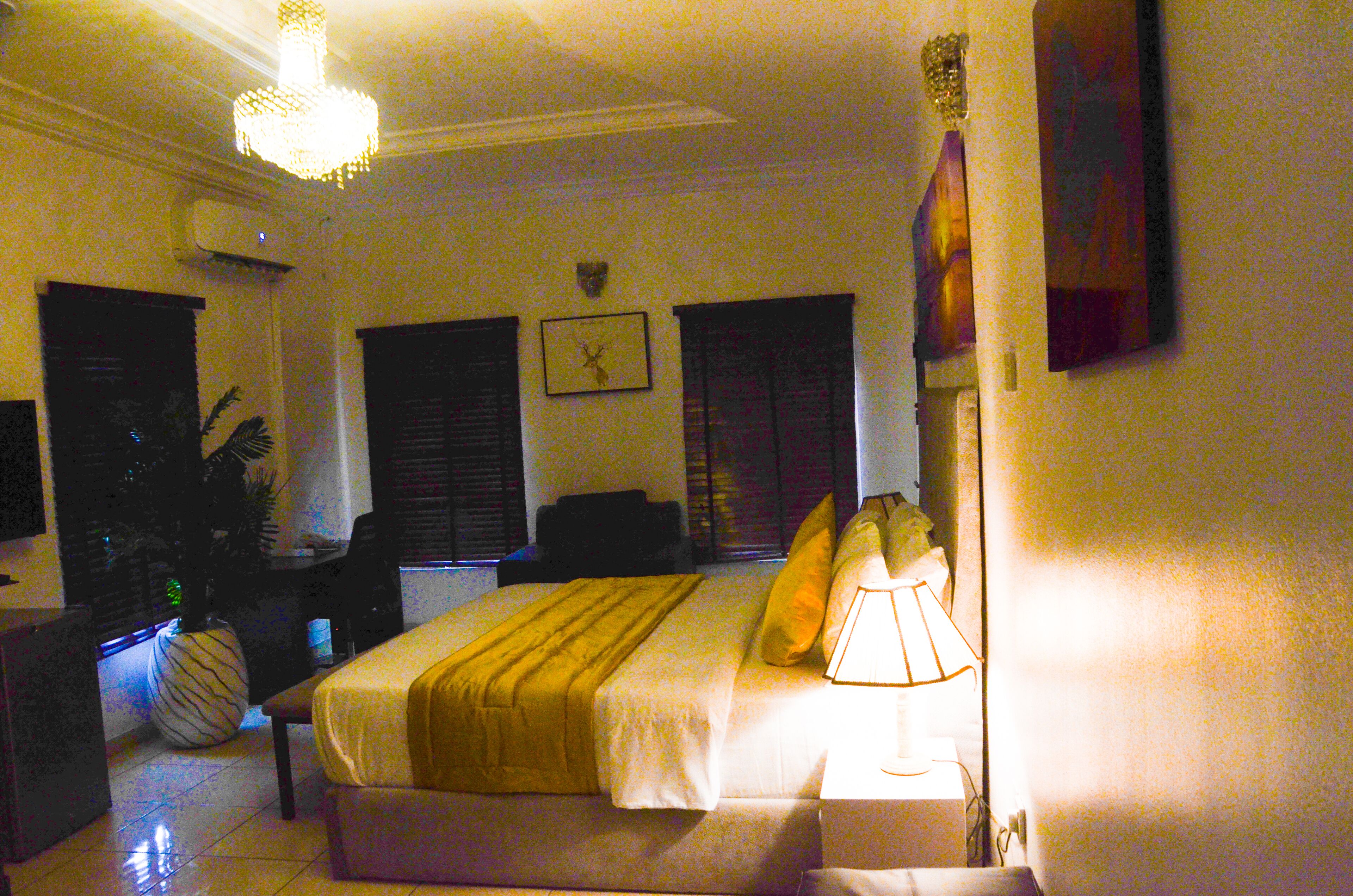 A hotel room with a bed, bedside table, lamp, and a wall clock.