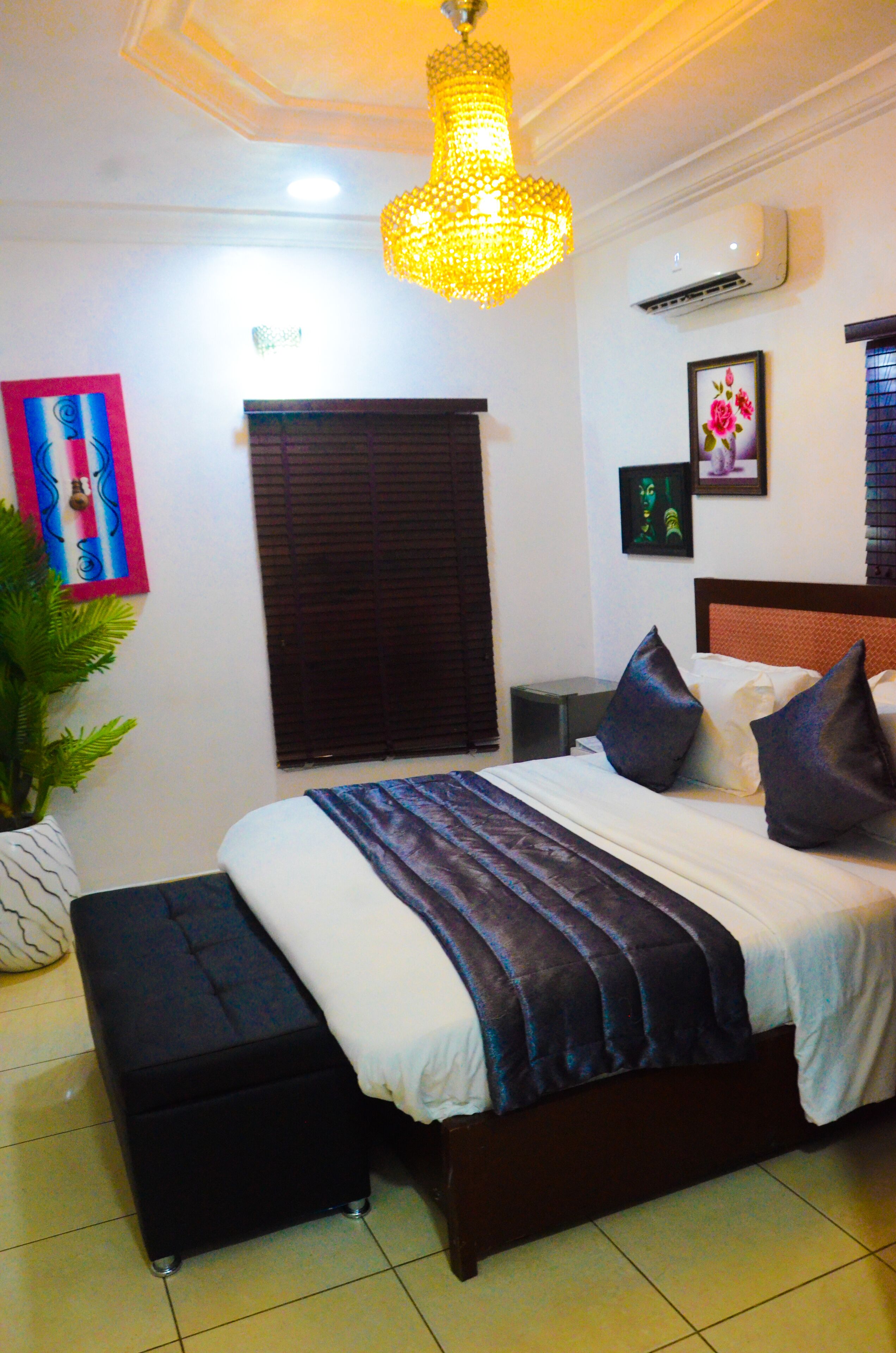 A neatly arranged bedroom with a bed, bedside tables, a bench, a potted plant, and a ceiling light fixture.