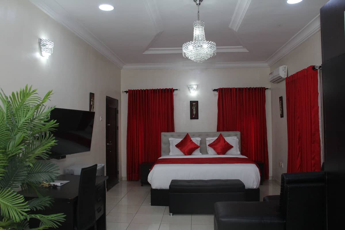 A hotel room with a bed, a desk, a chair, a TV, and a chandelier.