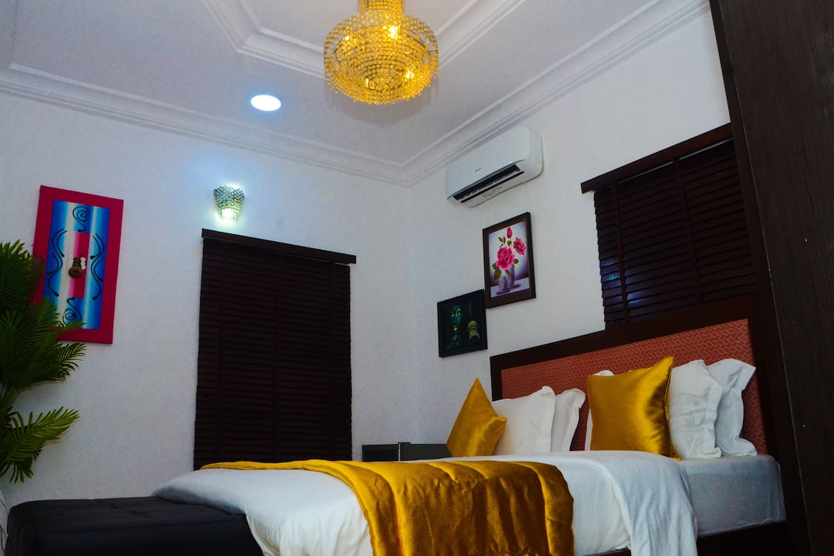 A hotel room with a bed, a chandelier, an air conditioner, and artwork on the walls.