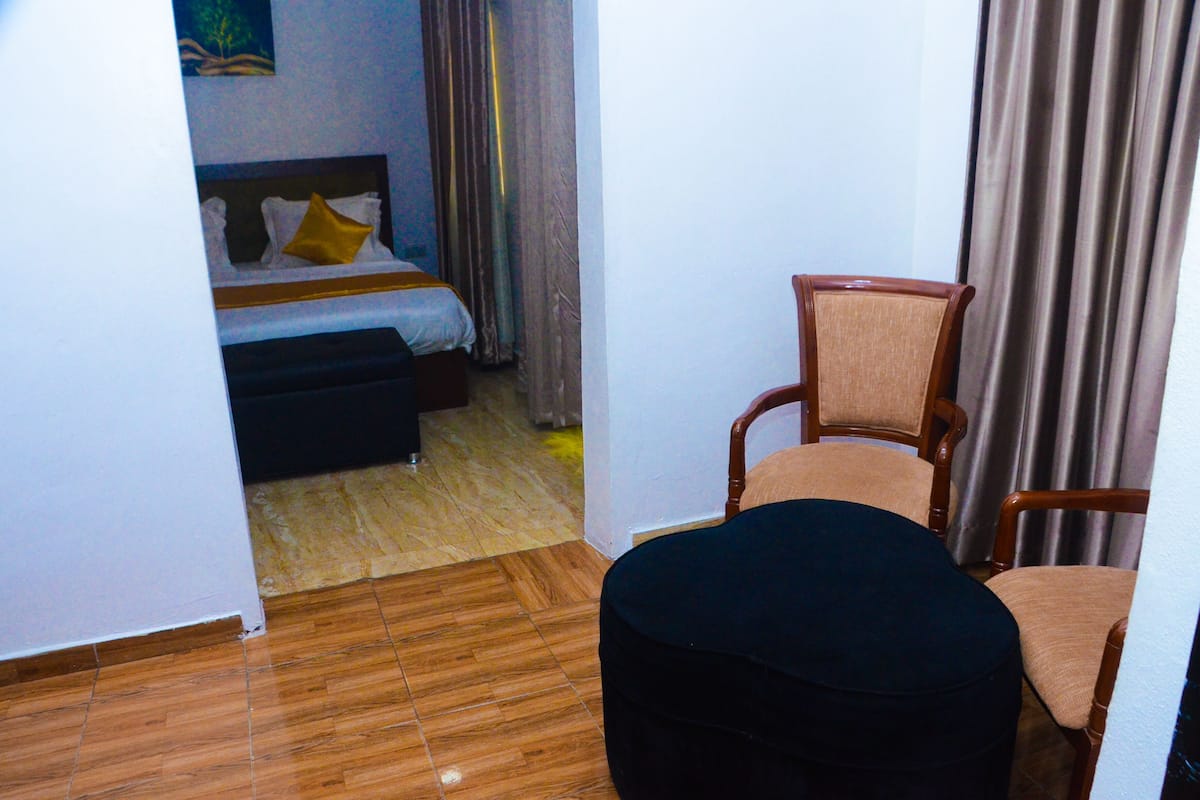 A hotel room with a bed, a chair, a small table, and a wooden floor.