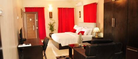 A hotel room with a bed, a desk, a chair, a sofa, and a wardrobe.